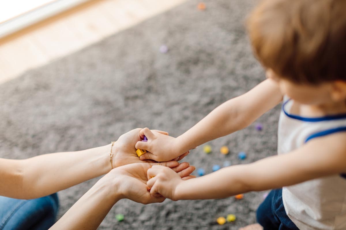 Odgojiteljica drži dijete za ruke tijekom igre na tepihu